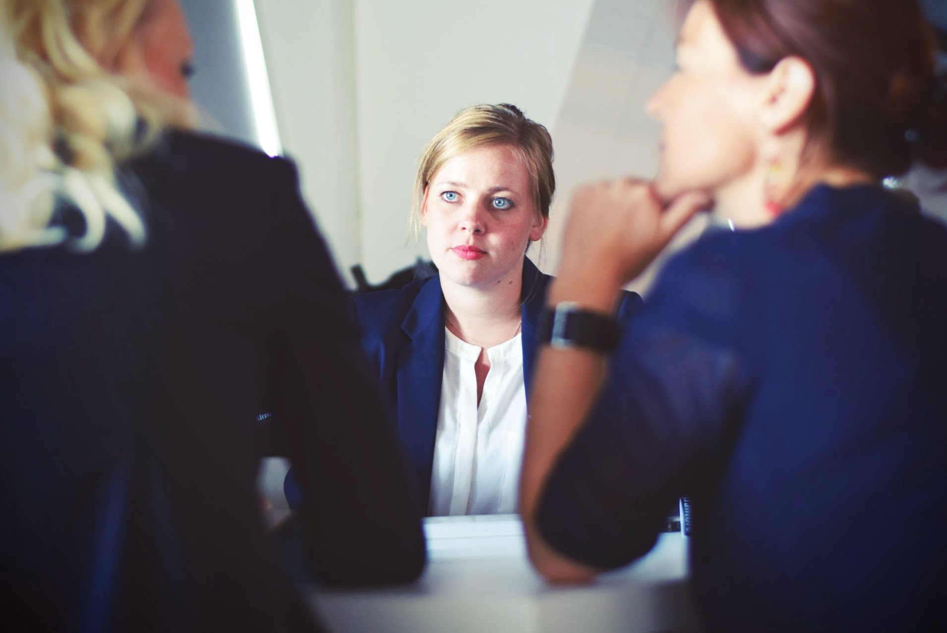 2 Women talking on 1 side of a table while facing a 3rd woman.