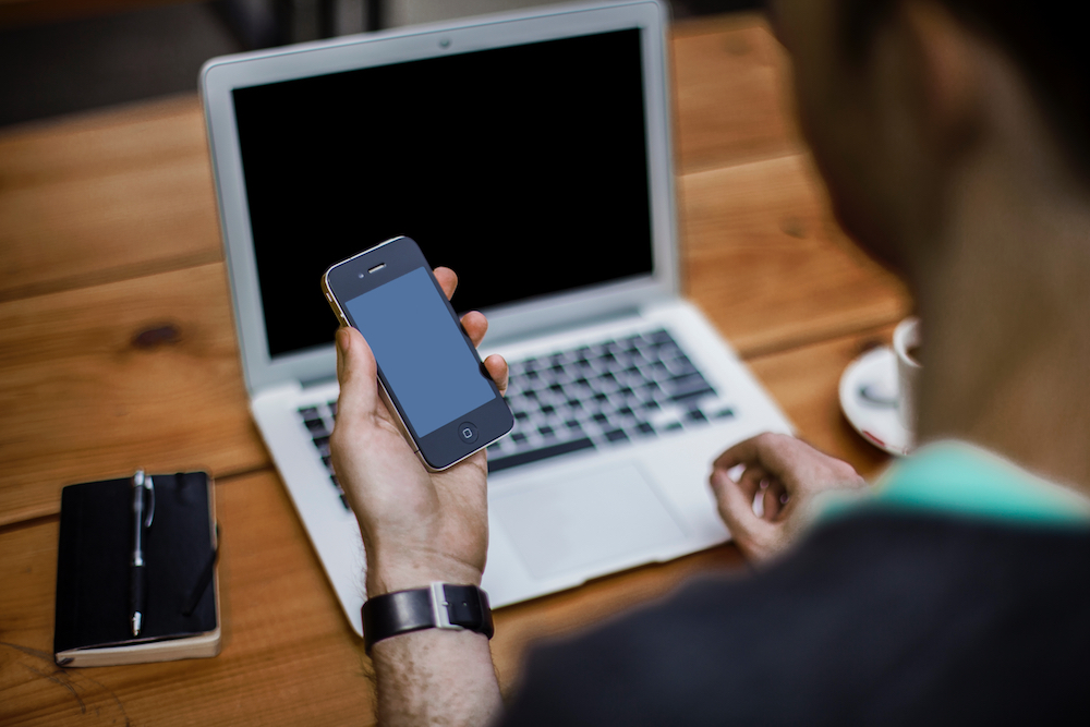 A man starting at a turned off iPhone 4 with laptop in the background.